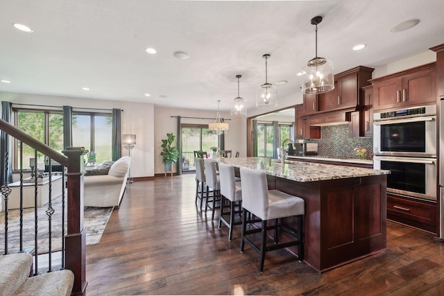 kitchen with decorative backsplash, sink, hanging light fixtures, a kitchen island with sink, and stainless steel double oven