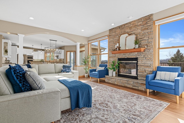 living room with a stone fireplace, a notable chandelier, ornate columns, and light hardwood / wood-style flooring