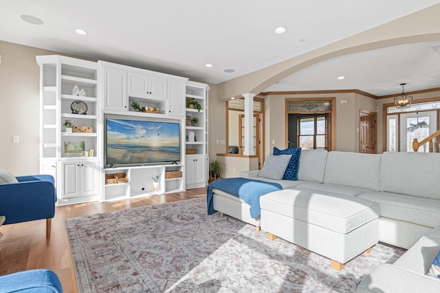 living room with decorative columns, an inviting chandelier, crown molding, and light hardwood / wood-style flooring