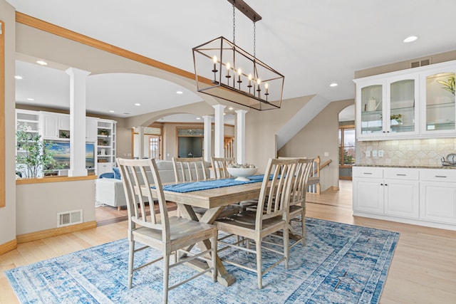 dining space with an inviting chandelier, decorative columns, a healthy amount of sunlight, and light hardwood / wood-style floors