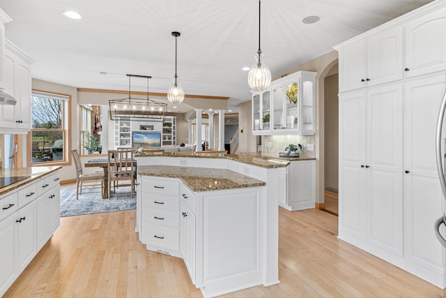 kitchen featuring light hardwood / wood-style floors, white cabinetry, tasteful backsplash, dark stone countertops, and pendant lighting