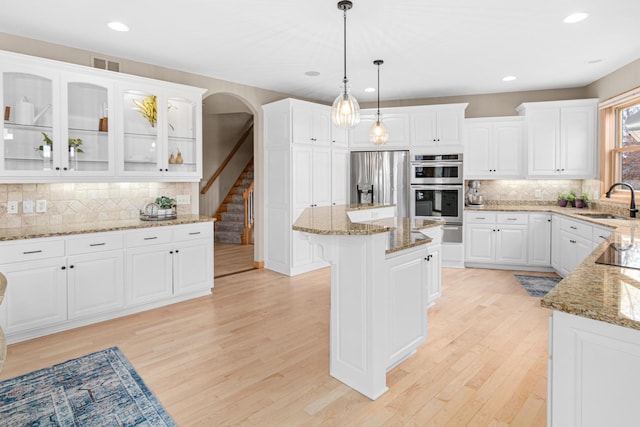 kitchen with stainless steel appliances, a kitchen island, white cabinetry, decorative light fixtures, and light hardwood / wood-style floors