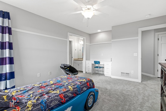 carpeted bedroom with built in desk, ceiling fan, and connected bathroom