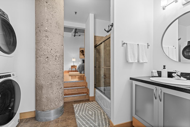 bathroom featuring vanity, stacked washer and dryer, tile patterned flooring, and bath / shower combo with glass door