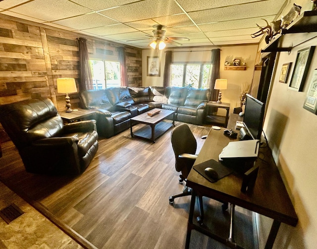 living room with hardwood / wood-style floors, a drop ceiling, a healthy amount of sunlight, and wood walls