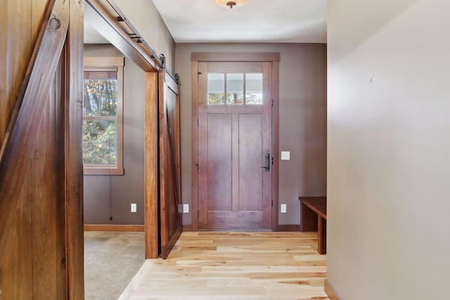 doorway with a barn door, a textured ceiling, and light hardwood / wood-style flooring