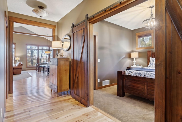 hallway with a wealth of natural light, light hardwood / wood-style floors, vaulted ceiling, and an inviting chandelier