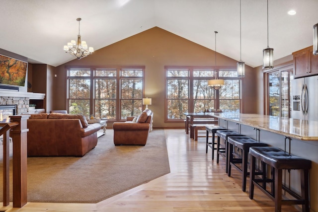 living room with a fireplace, a chandelier, light wood-type flooring, and high vaulted ceiling