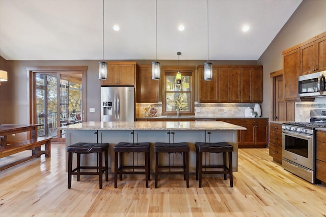 kitchen featuring a kitchen island, backsplash, light stone countertops, appliances with stainless steel finishes, and decorative light fixtures