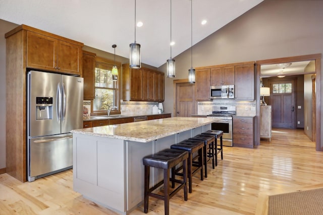 kitchen with high vaulted ceiling, light wood-type flooring, appliances with stainless steel finishes, and a center island