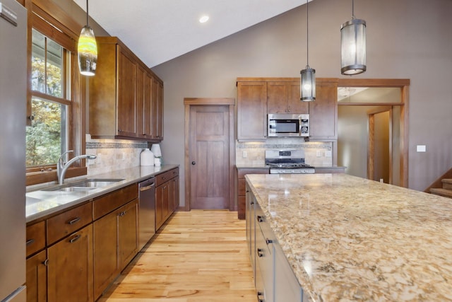 kitchen featuring stainless steel appliances, sink, backsplash, pendant lighting, and light hardwood / wood-style flooring