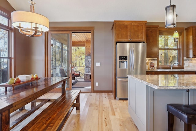 kitchen with light hardwood / wood-style floors, sink, light stone countertops, stainless steel fridge with ice dispenser, and pendant lighting