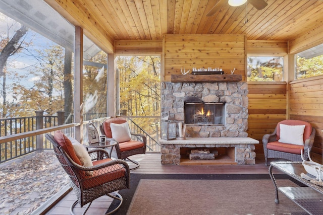 sunroom featuring a stone fireplace, wooden ceiling, and ceiling fan