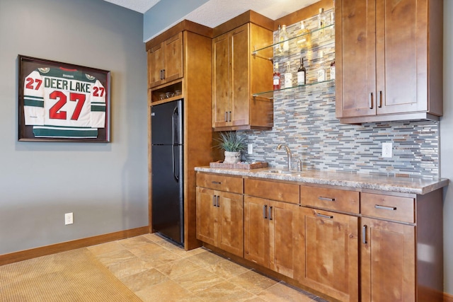 kitchen featuring black fridge, sink, light stone countertops, a textured ceiling, and backsplash