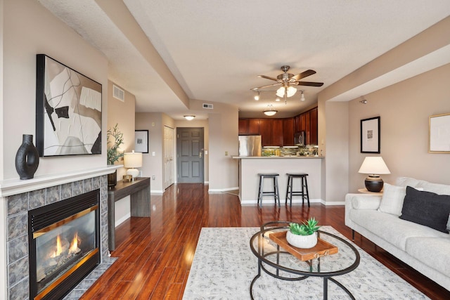 living room with a textured ceiling, ceiling fan, dark wood-type flooring, and a tiled fireplace