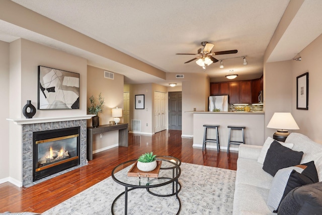 living room featuring a textured ceiling, ceiling fan, dark hardwood / wood-style flooring, and a fireplace