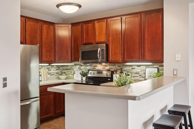 kitchen with a textured ceiling, appliances with stainless steel finishes, tasteful backsplash, kitchen peninsula, and a breakfast bar area