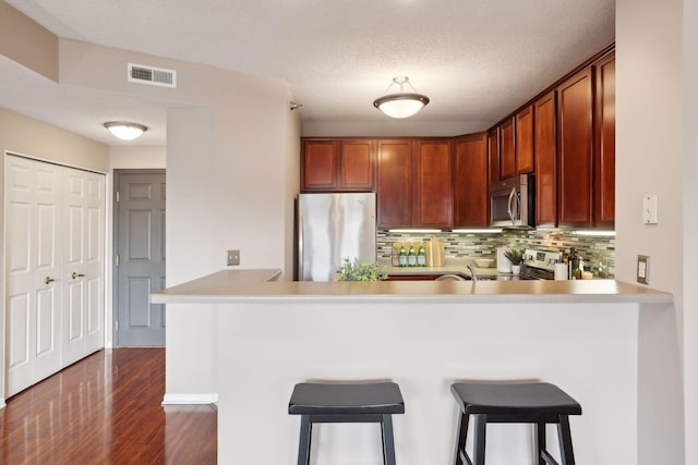 kitchen featuring kitchen peninsula, a breakfast bar, stainless steel appliances, and dark wood-type flooring