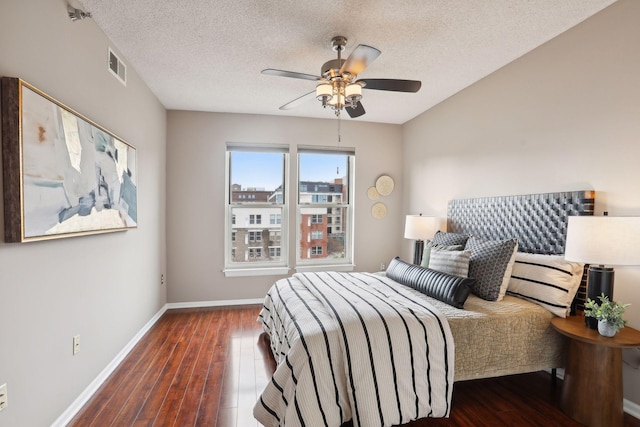 bedroom with a textured ceiling, ceiling fan, and dark wood-type flooring