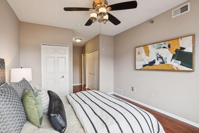 bedroom featuring dark hardwood / wood-style flooring, two closets, and ceiling fan