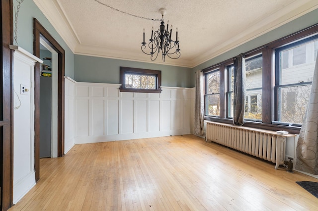 unfurnished dining area with a textured ceiling, light hardwood / wood-style flooring, radiator heating unit, and a chandelier