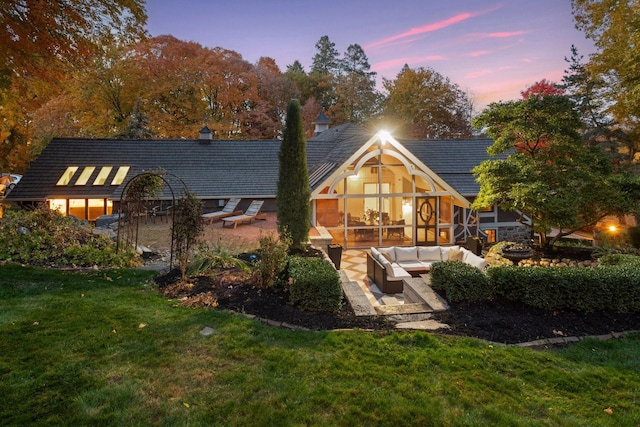 back house at dusk with a patio area, an outdoor living space, and a lawn