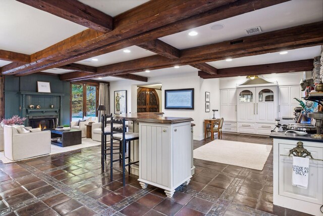 kitchen with beam ceiling, a center island, white cabinets, and a large fireplace