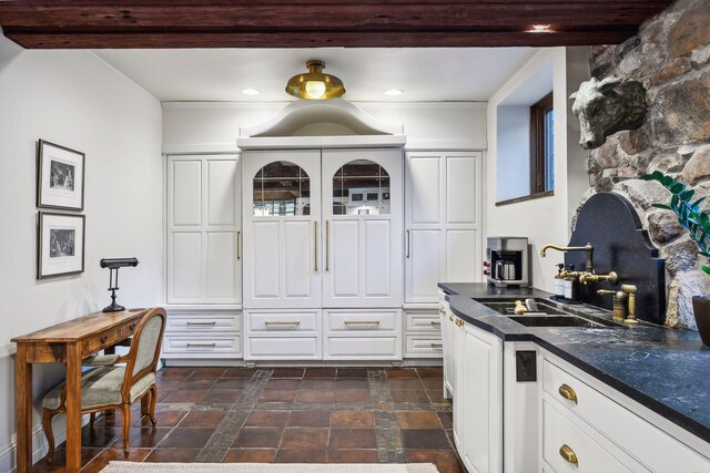 kitchen featuring crown molding, white cabinetry, beam ceiling, and sink