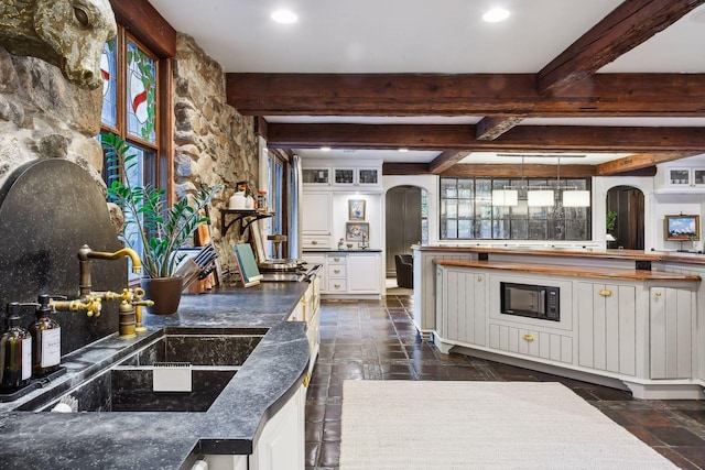 kitchen with beam ceiling, black microwave, sink, pendant lighting, and white cabinetry