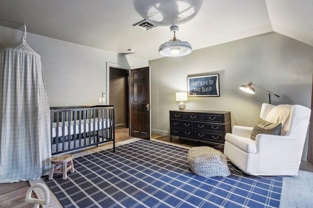 bedroom featuring lofted ceiling, hardwood / wood-style floors, and a nursery area