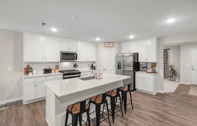 kitchen with a kitchen island with sink, dark wood-type flooring, sink, appliances with stainless steel finishes, and white cabinetry