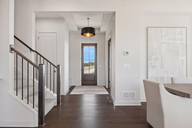 foyer entrance with dark wood-style floors, baseboards, stairway, and visible vents