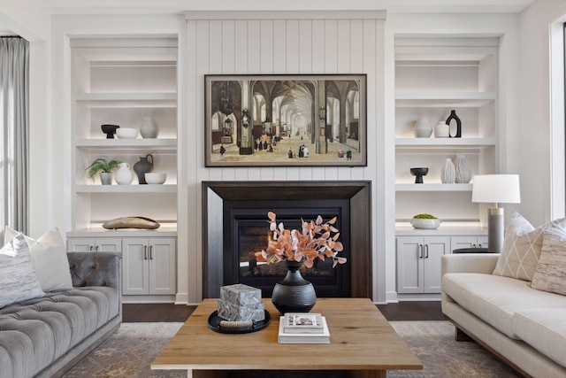 living area with dark wood-style flooring, a glass covered fireplace, and built in features