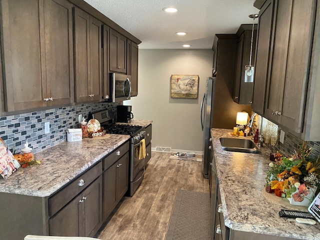 kitchen with dark brown cabinets, stainless steel appliances, sink, light hardwood / wood-style floors, and tasteful backsplash