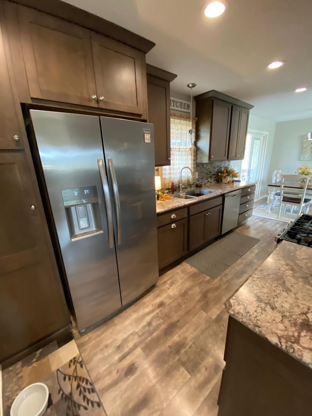 kitchen with tasteful backsplash, appliances with stainless steel finishes, sink, light hardwood / wood-style floors, and decorative light fixtures