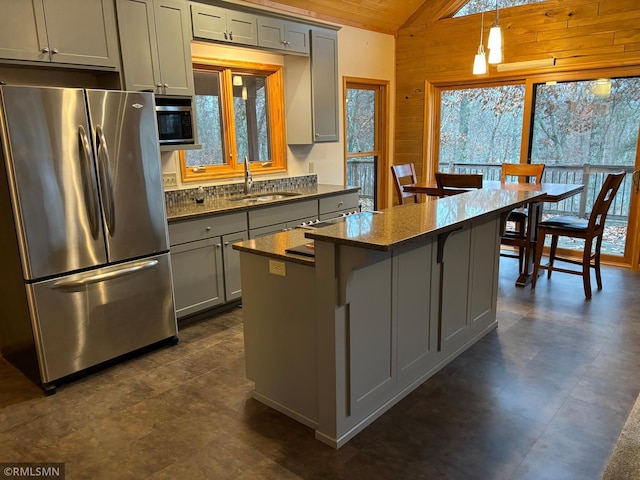 kitchen with lofted ceiling, wood walls, sink, gray cabinetry, and stainless steel appliances