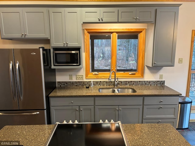 kitchen with stainless steel appliances, sink, dark stone counters, and a wealth of natural light