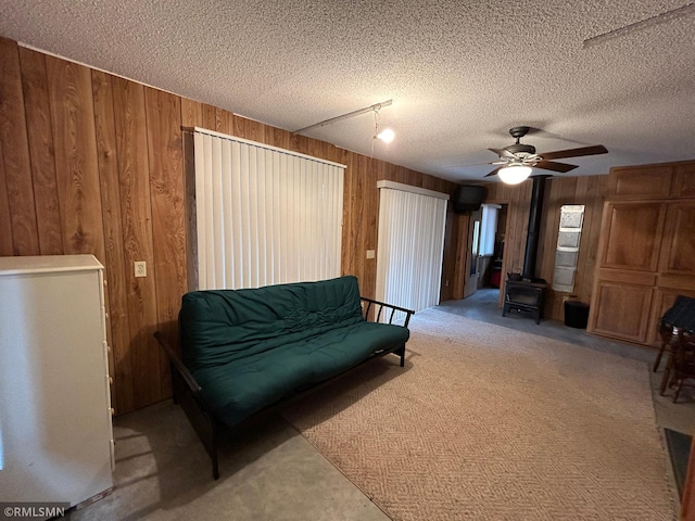 living area featuring a textured ceiling, wooden walls, light colored carpet, and ceiling fan