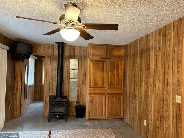 unfurnished living room with wood walls, a textured ceiling, a wood stove, and ceiling fan