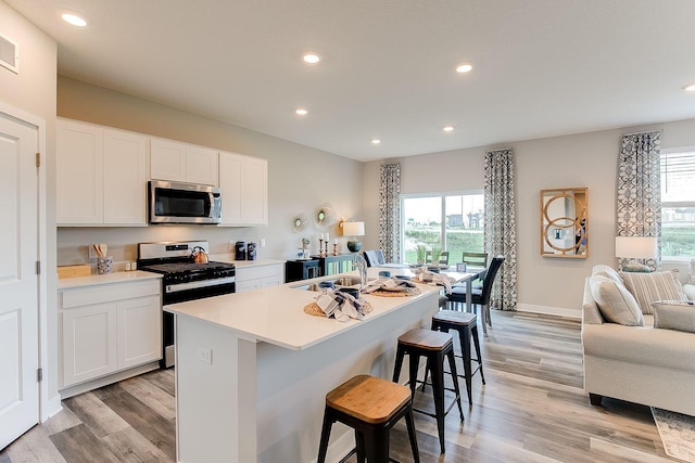 kitchen with stove, a kitchen island with sink, a healthy amount of sunlight, and white cabinets