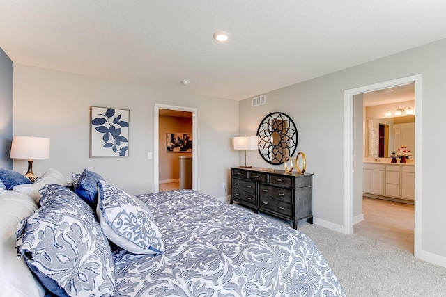 bedroom with ensuite bathroom and light carpet