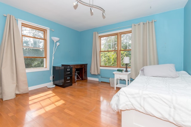 bedroom featuring light hardwood / wood-style flooring, a baseboard radiator, and multiple windows