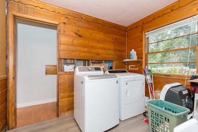 washroom featuring washing machine and clothes dryer, wooden walls, and light hardwood / wood-style flooring