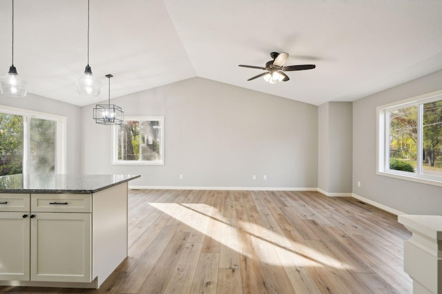 kitchen with hanging light fixtures, white cabinetry, lofted ceiling, dark stone counters, and light hardwood / wood-style flooring