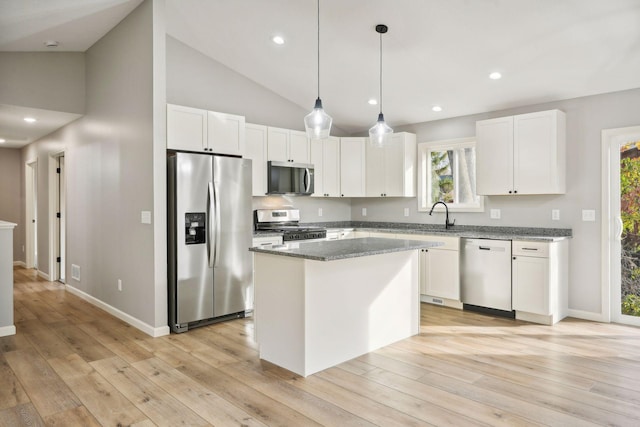 kitchen featuring appliances with stainless steel finishes, a center island, light hardwood / wood-style floors, dark stone counters, and white cabinets