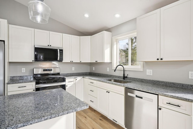 kitchen featuring appliances with stainless steel finishes, sink, vaulted ceiling, white cabinets, and light hardwood / wood-style flooring