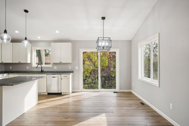 kitchen featuring light wood-type flooring, vaulted ceiling, decorative light fixtures, stainless steel dishwasher, and white cabinets