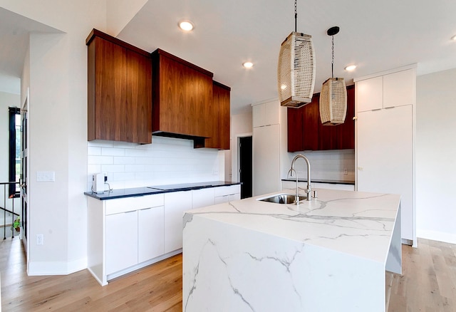 kitchen with sink, light hardwood / wood-style floors, decorative light fixtures, decorative backsplash, and a center island with sink