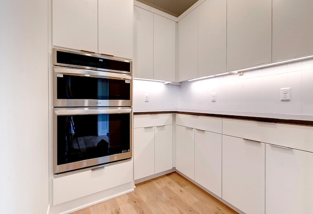 kitchen featuring light hardwood / wood-style floors, white cabinetry, double oven, and tasteful backsplash