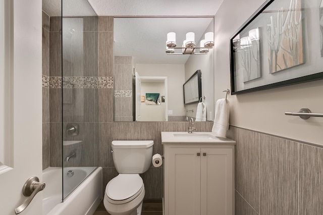 full bathroom featuring vanity, tiled shower / bath, toilet, a textured ceiling, and tile walls